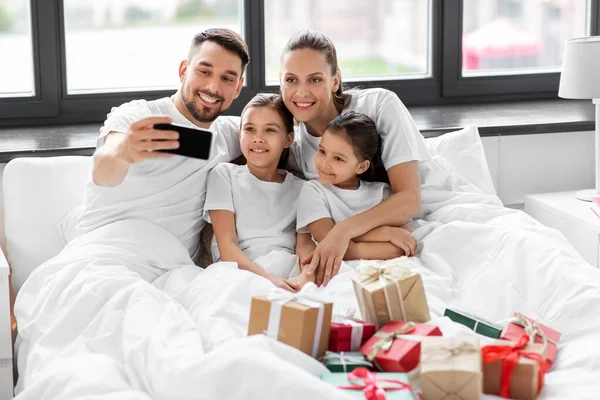 Família com presentes de Natal tomando selfie na cama — Fotografia de Stock