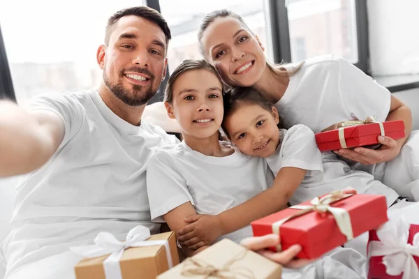 Familia con regalos de Navidad tomando selfie en la cama —  Fotos de Stock