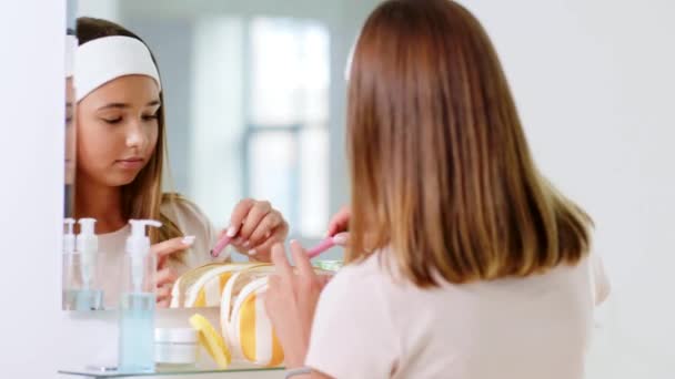 Teini tyttö soveltamalla huulikiiltoa kylpyhuoneessa — kuvapankkivideo