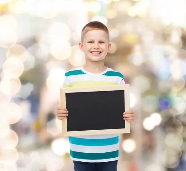 Улыбающийся маленький мальчик держит пустую черную доску — стоковое фото
