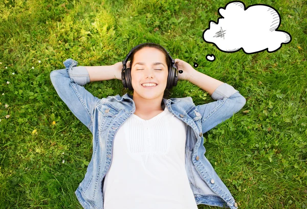Lachende jong meisje in hoofdtelefoon liggen op gras — Stockfoto