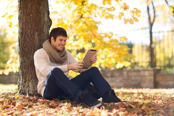 Улыбающийся молодой человек с планшетным ПК в осеннем парке — стоковое фото