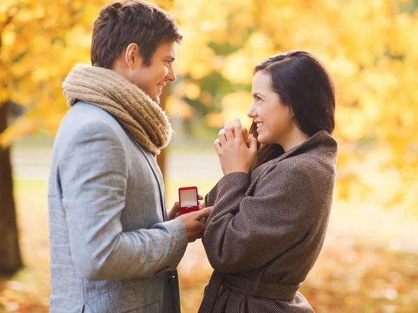 Coppia sorridente con confezione regalo rossa nel parco autunnale — Foto Stock