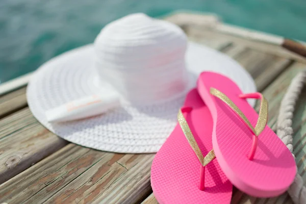 Close up of hat, sunscreen and slippers at seaside — Stock Photo, Image