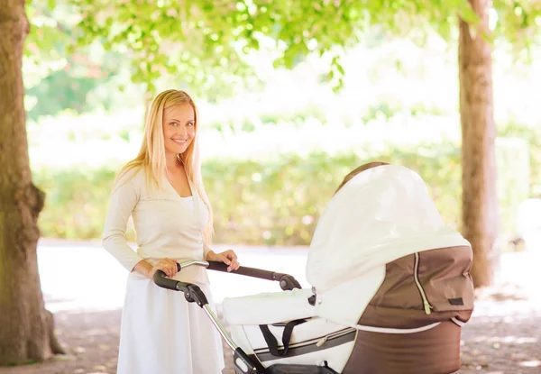 Gelukkig moeder met wandelwagen in park — Stockfoto