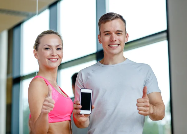 Smiling young woman with personal trainer in gym — Stock Photo, Image