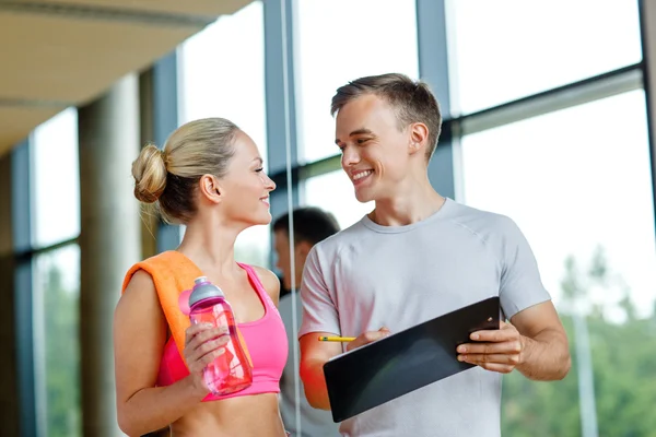 Smiling young woman with personal trainer in gym — Stock Photo, Image