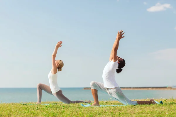 Pareja sonriente haciendo ejercicios de yoga al aire libre —  Fotos de Stock