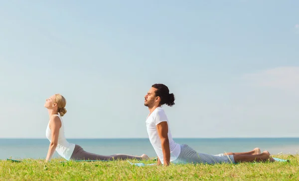 smiling couple making yoga exercises outdoors