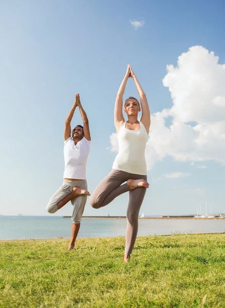 Sorrindo casal fazendo exercícios de ioga ao ar livre — Fotografia de Stock