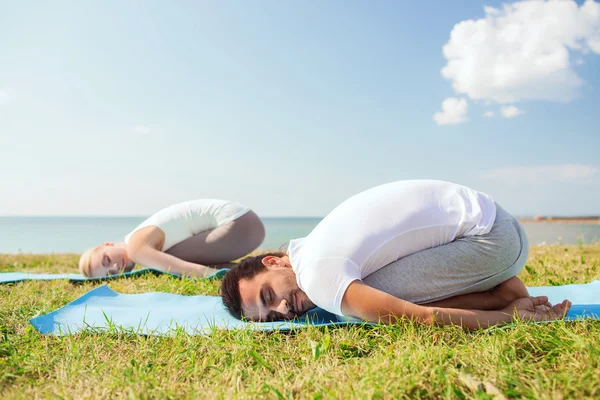 Sorrindo casal fazendo exercícios de ioga ao ar livre — Fotografia de Stock
