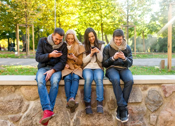 Smiling friends with smartphones in city park — Stock Photo, Image