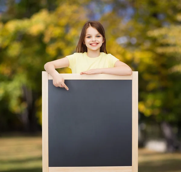 Happy little girl pointing finger to blackboard — Stock Photo, Image