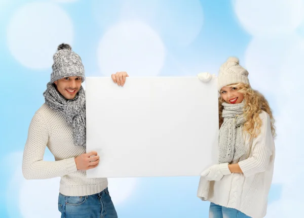 Casal sorridente em roupas de inverno com placa em branco — Fotografia de Stock