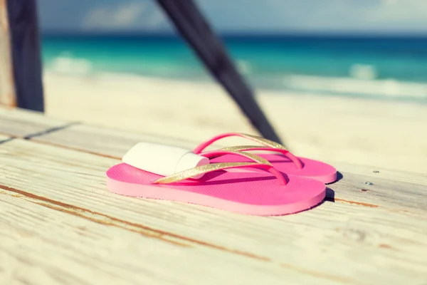 Primo piano di crema solare e pantofole al mare — Foto Stock