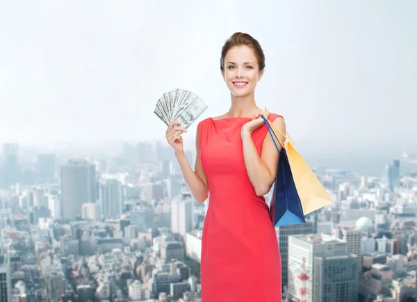 Mulher sorridente em vestido vermelho com sacos de compras — Fotografia de Stock