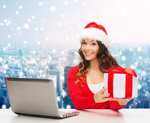 Lachende vrouw in kerstmuts met een geschenk en laptop — Stockfoto