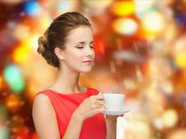 Улыбающаяся женщина в красном платье с чашкой кофе — стоковое фото