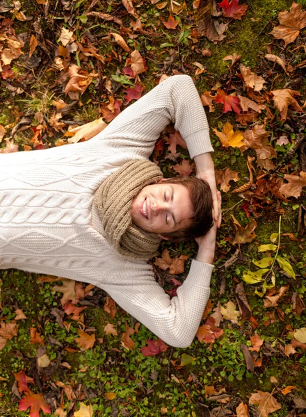 Улыбающийся молодой человек лежит на земле в осеннем парке — стоковое фото