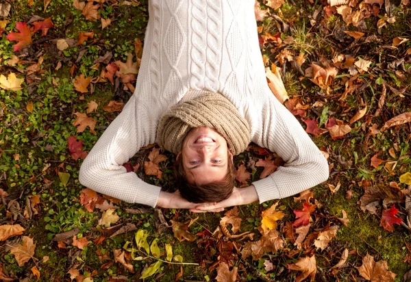 Усміхнений молодий чоловік лежить на землі в осінньому парку — стокове фото