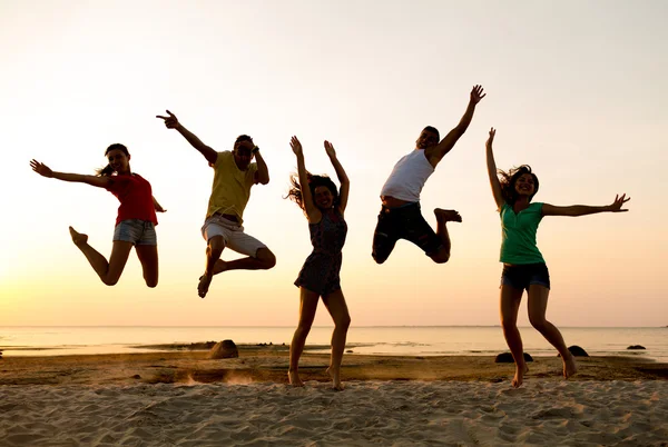 Lächelnde Freunde tanzen und springen am Strand — Stockfoto