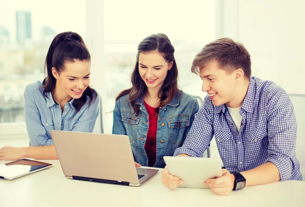 Drie lachende studenten met laptop en tablet pc — Stockfoto