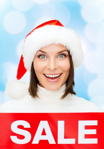 Sorrindo mulher em santa chapéu auxiliar com sinal de venda — Fotografia de Stock