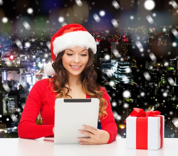 Smiling woman in santa hat with gift and tablet pc — Stock Photo, Image