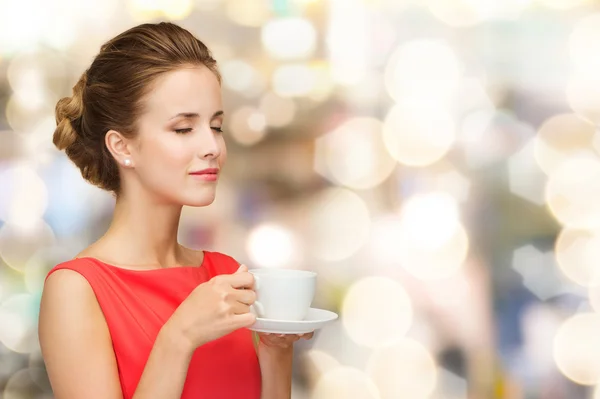 Улыбающаяся женщина в красном платье с чашкой кофе — стоковое фото