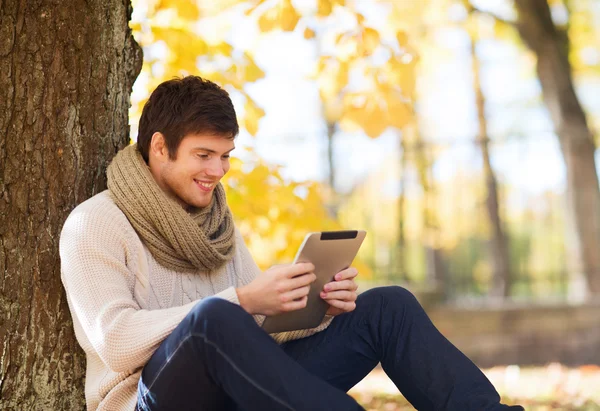 Glimlachend jongeman met de tablet pc in de herfst park — Stockfoto