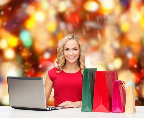 Mulher sorridente em camisa vermelha com presentes e laptop — Fotografia de Stock