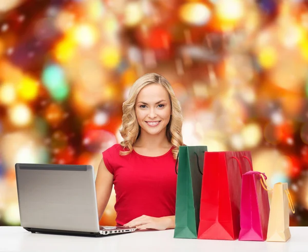 Smiling woman in red shirt with gifts and laptop — Stock Photo, Image