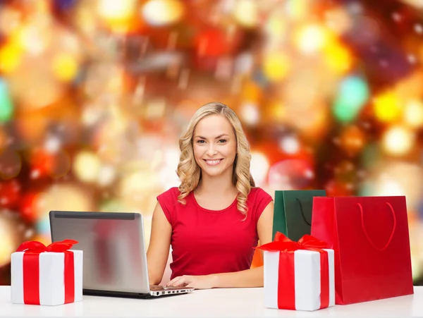 Smiling woman in red shirt with gifts and laptop — Stock Photo, Image