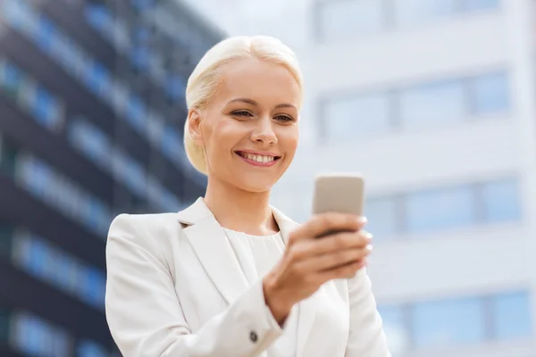 Улыбающаяся деловая женщина со смартфоном на открытом воздухе — стоковое фото