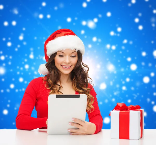 Lachende vrouw in kerstmuts met een geschenk en tablet pc — Stockfoto