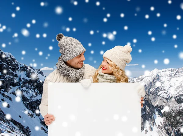 Casal sorridente em roupas de inverno com placa branca — Fotografia de Stock