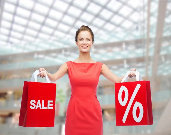 Mujer joven en vestido rojo con bolsas de compras — Foto de Stock