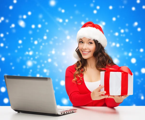 Lachende vrouw in kerstmuts met een geschenk en laptop — Stockfoto