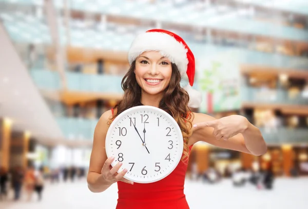 与时钟微笑在圣诞老人的助手帽子的女人 — 图库照片