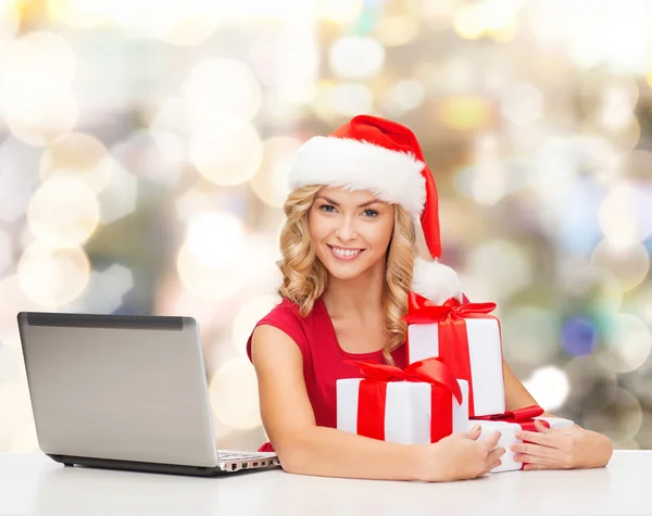 Donna sorridente in cappello di Babbo Natale con regali e laptop — Foto Stock