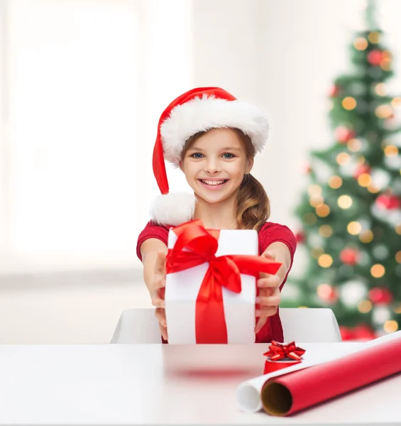 Chica sonriente en sombrero de ayudante de santa con caja de regalo — Foto de Stock