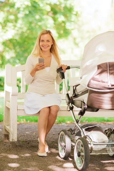 Happy mother with smartphone and stroller in park — Stock Photo, Image