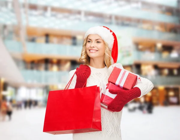 Souriant jeune femme dans santa chapeau d'aide avec des cadeaux — Photo