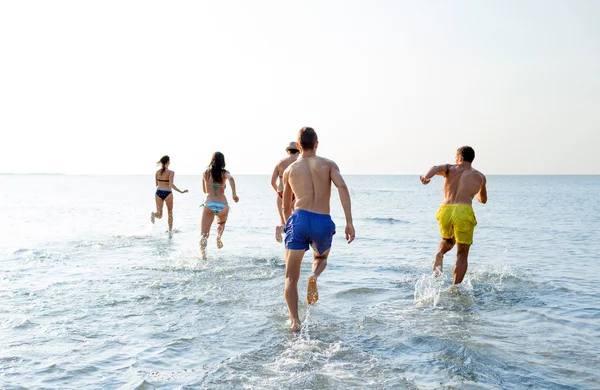 Amigos sonrientes corriendo en la playa desde atrás — Foto de Stock