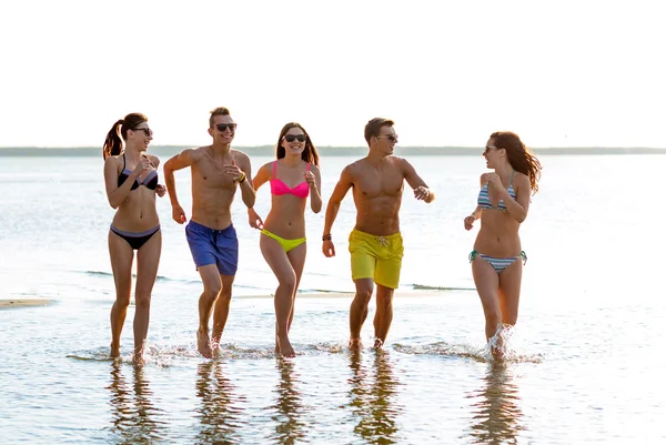 Amigos sonrientes en gafas de sol corriendo en la playa —  Fotos de Stock