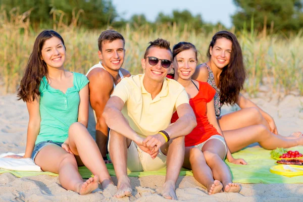 Smiling friends sitting on summer beach — Stock Photo, Image