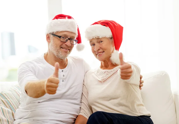 Feliz casal sênior em santa helper chapéus em casa — Fotografia de Stock