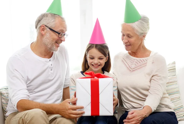 Família sorridente em chapéus de festa com caixa de presente em casa — Fotografia de Stock