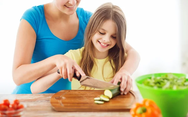 Sorrindo menina com a mãe cortando pepino — Fotografia de Stock
