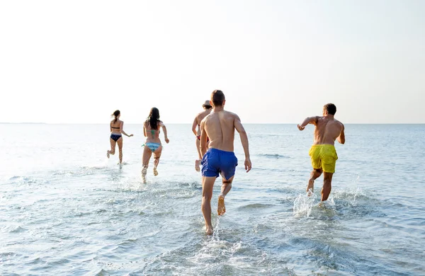 Uśmiechnięty znajomych działa na plaży z powrotem — Zdjęcie stockowe